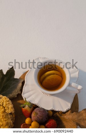 Overhead of various fruits, autumn leaves and cup of green tea on chopping board
