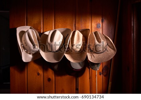 Four cowboy hats hung in row on wooden paneled wall Royalty-Free Stock Photo #690134734