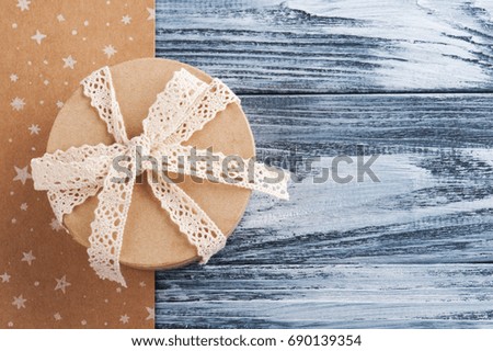Hand crafted gift with lace bow, on kraft and blue wooden background