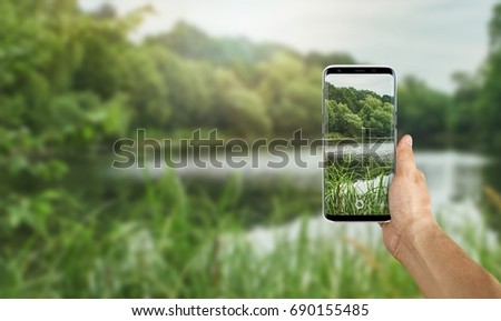 Tourist taking a picture of wild lake using a smartphone, point of view shot