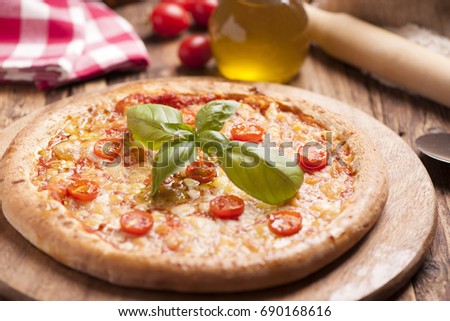 Italian pizza with tomato topped with melted golden cheese, herbs and basil served on a round wooden board on an old wood table