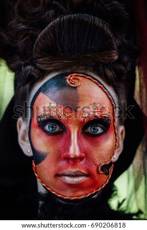 Close-up beauty red art make-up portrait of halloween woman Witch baroque. Face like Victorian-Venetian Mask. Dark evil force. Professional complex work of the makeup artist-stylist.