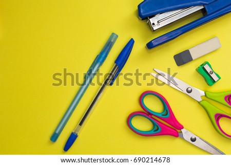 School accessories on a yellow background. Scissors, pens, sharpener, stapler.