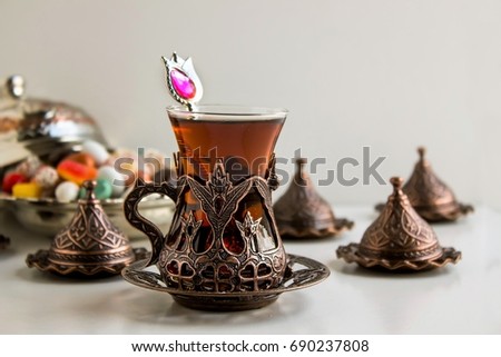 Traditional Turkish Tea in vintage cooper glass on white surface with colorful candies.Festival concept
