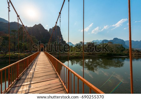 Picture of orange bridge over the Nam Song River with tropical vegetation. Close to Tham Chang Cave in the city of Vang Vieng, Laos.