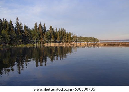 Waskesiu Lake shoreline with woods in the background and shimmering reflection on the water.
