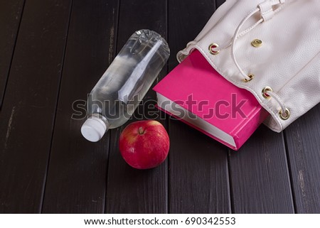 White leather backpack, pink book, bottle of water on a black background