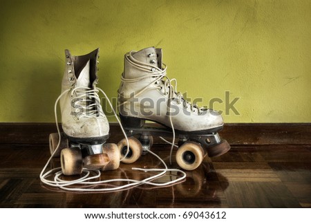 Old worn roller skates with big shoe-laces on a yellow wall background