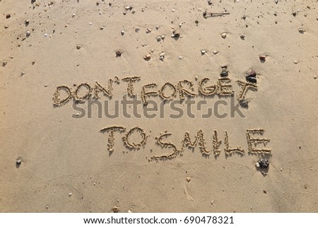 Handwriting  words "DON'T FORGET TO SMILE" on sand of beach.