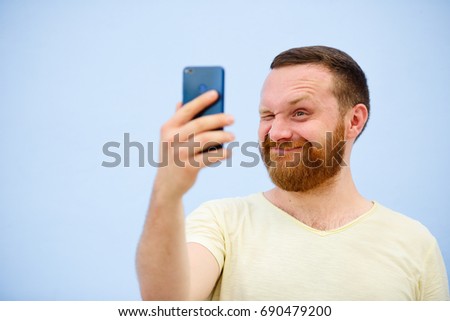Cheerful bearded Man winks at the phone, suitable for advertising, on a blue background.