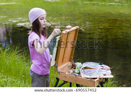 A girl in a pink T-shirt is painting a picture in nature. Drawing artist oil paints.
