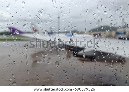 Blurred rain drops on aircraft window, passenger's view from inside of an airplane, water spray on window surface of an aircraft, cloudy day at the airport