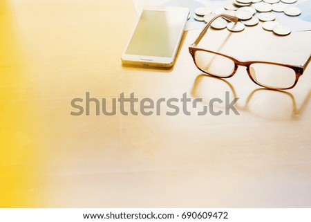 Concept of financial and economics. Smart phone, Coins and glasses on wooden table