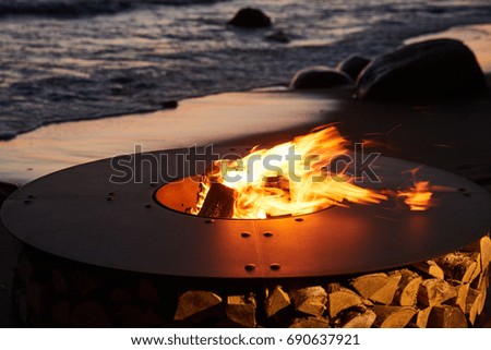 The beautiful metal round a fireplace, a brazier, costs on the Sandy Coast with a tidal wave at sunset, stones, sand, waves, the landscape, tranquillity, the sun falls, firewood, nobody