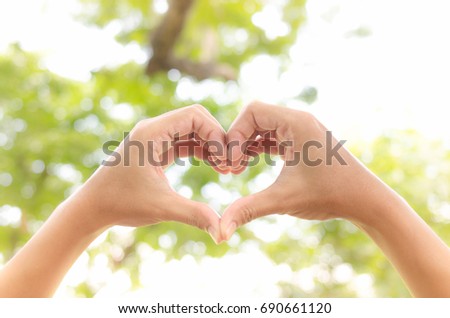 Hands with heart sign on green blur at garden background. Royalty-Free Stock Photo #690661120