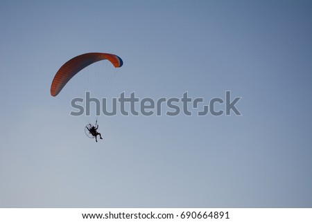 Silhouette of a male paraglider on a paraplan against a background of a sunset in the sky and clouds hovering over the sea. 