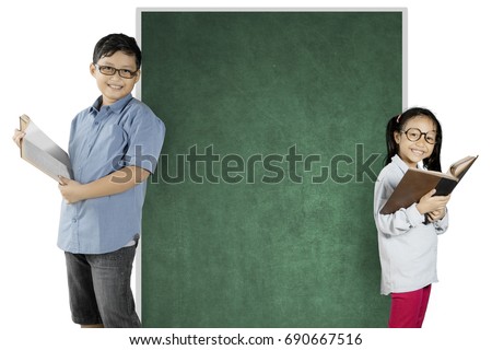 Two nerdy students reading a book while standing near a blank chalkboard, isolated on white background