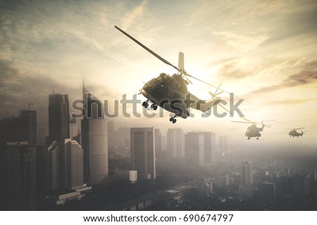 Silhouette of three army helicopters doing patrols while flying over downtown, shot at sunset time Royalty-Free Stock Photo #690674797