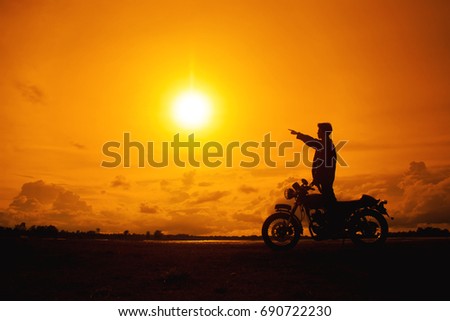 Silhouette of biker man with his motorbike beside the natural lake and beautiful, enjoying freedom and active lifestyle, having fun on a bikers tour.sunset background and sky.