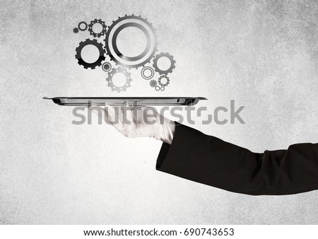 Crank wheel machine working concept with racks served on silver plate by hand in white glove and industrial grey wall pattern background.