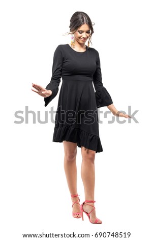 Pretty cute fashion model in black dress walking and balancing looking down.  Full body length portrait isolated on white studio background. 