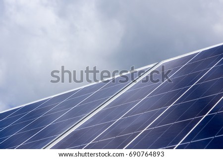 Blue solar panels against background of sky with clouds
