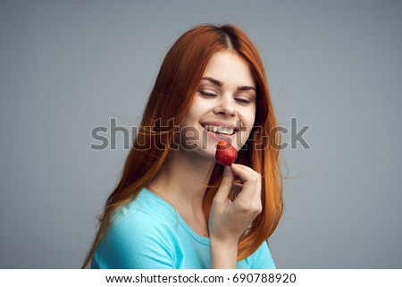 Woman smiling and holding a strawberry on a gray background                               