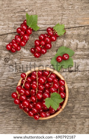 Red currant berries in a wooden bowl with leaf on the old wooden background. Top view