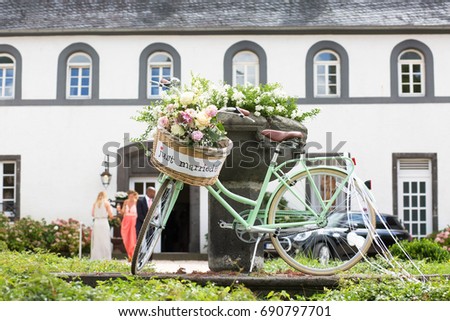 Mint color vintage bicycle with the words "just married" and basket full of beautiful flowers (english roses, succulents and green) before the wedding location. Natural light, selective focus.