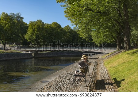 Woman sitting a park bench and reading a newspaper 