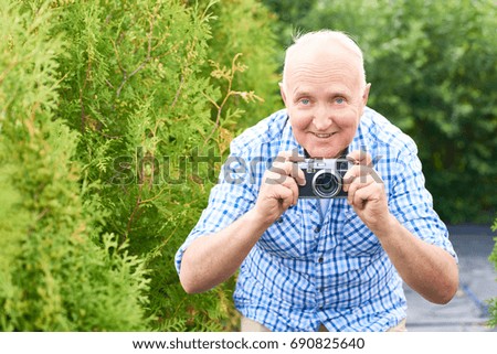 Portrait of smiling senior man taking pictures in park using vintage photo camera while travelling