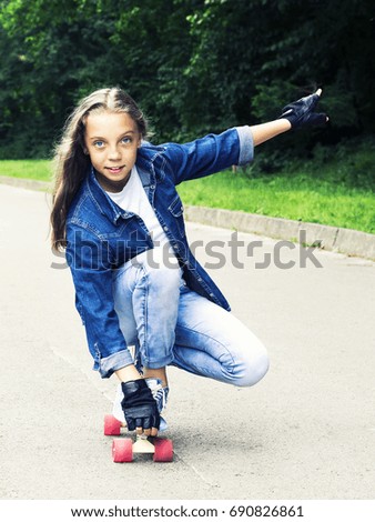 Beautiful blonde teen girl in jeans shirt, on skateboard in park