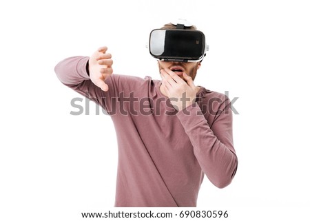 Portrait of young amazed man using virtual reality glasses on white background. Thoughtful boy playing with visual reality glasses isolated