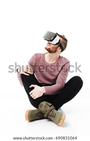 Young man sitting in studio and using virtual reality glasses on white background. Cool boy playing with visual reality glasses isolated