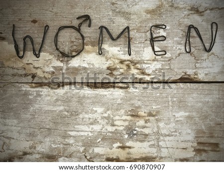 Iron women text made from steel wire. One letter is placed with female symbol. Bent metal text placed on wooden rustic and old surface. Empty space on down side for own texture or information