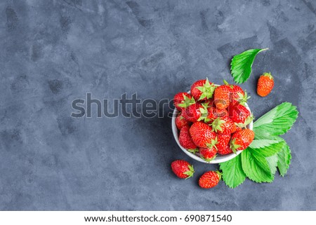 Ripe strawberry in a white bowl on concrete background. Top view space for text.