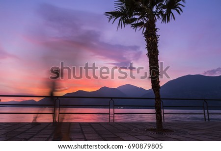 Beautiful foggy sunset at Iseo lake, Lombardy, Italy. Silhouettes of people walking on promenade street in Iseo city. Lake Iseo or Lago d'Iseo or Sebino is the 4th largest lake in Lombardy