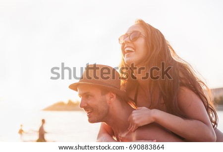 Young man piggybacking his girlfriend on the beach at sunset, golden hour