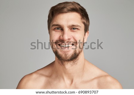 Portrait of a smiling young man with bare swimmers shoulders on a gray background, powerful, beard, charismatic, adult, brutal, athletic, edited photo, bright smile, white teeth smile, look in camera