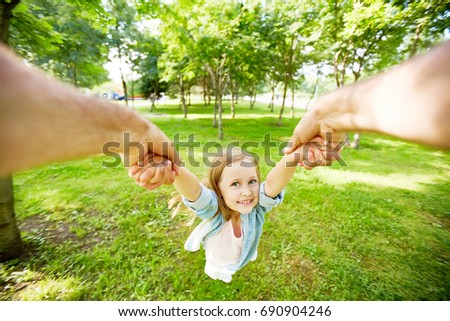 Joyful child being whirled by her parent in park on summer day Royalty-Free Stock Photo #690904246