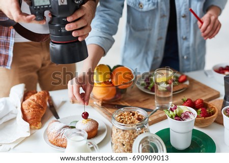 Photographer shooting food on the table while his assistant helping him