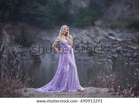 Attractive pretty woman in creative purple dress silhouette mermaid long lace train. Fantasy picture pregnancy blonde cute girl. Smiling happy face. Enjoying nature Park river rocks. Long curly hair