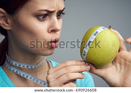 Woman wrapped an apple with a measuring tape on a gray background                               