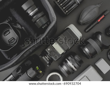 top view of work space photographer with mirrorless camera system, camera flash, battery charger, camera cleaning kit, memory card, and camera accessory on black table background