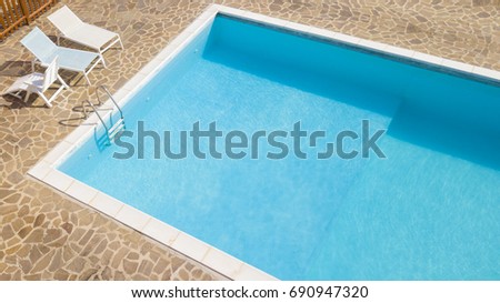 Aerial view of a blue pool with stairs to descend and climb into the water. Around marble tiles. There are empty loungers by the pool. The pool is part of a private villa. Royalty-Free Stock Photo #690947320