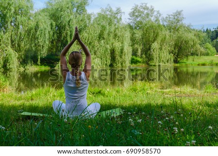 A young girl is engaged in yoga in a park near a lake in white clothes on a summer day, the concept of a healthy and athletic lifestyle