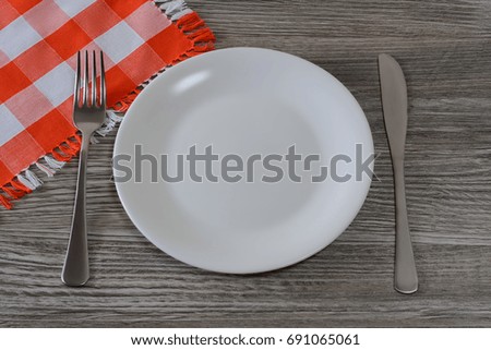 Empty white round plate, knife, fork and tablecloth on  wooden table. Top view photo