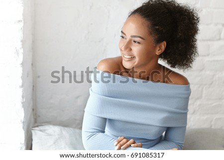 People, leisure and lifestyle. Picture of gorgeous young Afro American female student with perfect healthy skin and cute smile having rest at coffee shop, waiting for fiends to join her for lunch