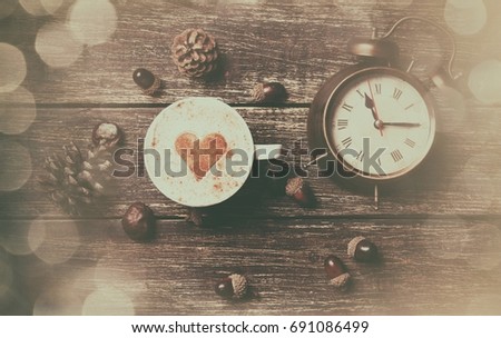 Cup of coffee with heart shape and pine cone with acorn and clock on wooden background
