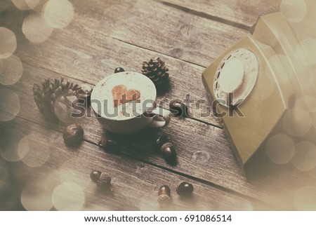 Cup of coffee with heart shape and green dial phone on wooden background